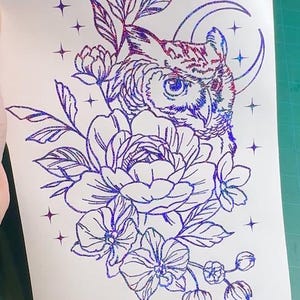 May include: A glittery, iridescent owl illustration with floral and celestial elements. The design features an owl perched amidst flowers, a crescent moon, and stars. The artwork is rendered in shades of purple, blue, and red, creating a shimmering effect.