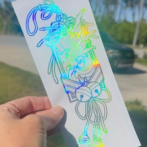 May include: A holographic sticker with a detailed design of a Japanese knot with bells and a wave pattern. The sticker is iridescent with rainbow colors.