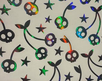 May include: A pattern of black cherries with skull faces and green leaves, interspersed with black stars. The cherries have a holographic, rainbow-colored effect. The design is on a white background.