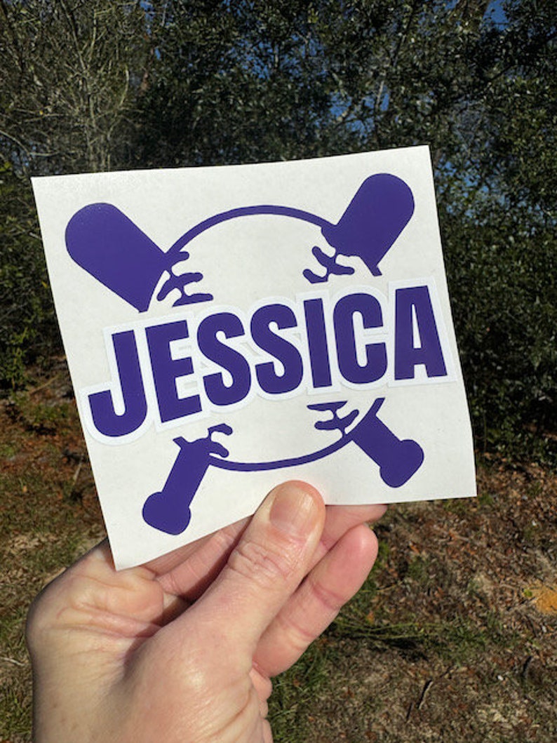 Op de afbeelding: Een witte sticker met een paars honkbal- en knuppelontwerp. De naam "JESSICA" is in paarse letters geschreven.