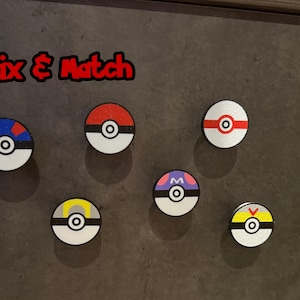 May include: Six circular drawer knobs featuring various colourful designs inspired by Poke Balls, each with a central button detail. The text Mix & Match is printed in red and black above the knobs, which include red, blue, yellow, and purple accents.