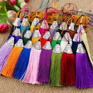 Puede incluir: Una colección de borlas coloridas con tapas plateadas en forma de campana. Las borlas son de varios colores, incluyendo morado, naranja, azul, rosa, verde y rojo. Cada borla tiene una cuerda para colgar.