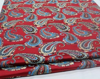 Könnte beinhalten: Roter Stoff mit Paisley-Muster in Blau, Gold und Schwarz. Der Stoff ist in der Mitte gefaltet und hat eine glänzende, satinartige Oberfläche.