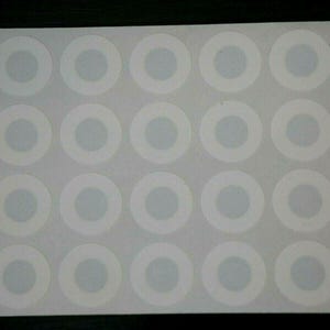 May include: A rectangular sheet of white adhesive labels featuring a grid of twenty circular stickers. Each sticker consists of a solid white outer ring surrounding a translucent or light grey circular centre, arranged in four rows of five stickers.