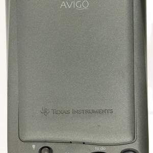 Op de afbeelding: Een grijze Texas Instruments Avigo PDA. Het apparaat heeft een opklapbare klep en verschillende knoppen met de tekst "open power", "address", "to do", "memo" en "schedule". Het apparaat heeft ook omhoog en omlaag pijlknoppen.