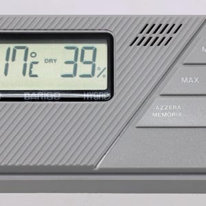 Pode incluir: Um termómetro e higrómetro digital cinzento com um ecrã preto que mostra 17°C e 39%. Possui botões vermelho, verde e preto com as etiquetas MIN, MAX e AZZERA MEMORIA. O dispositivo também mostra as palavras MEM, THERMO, BARIGO e HYDRO.