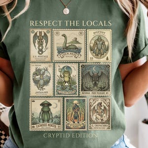 Puede incluir: Camiseta verde con el texto "Respect the Locals" y un diseño de sellos con temática de críptidos. Los sellos presentan ilustraciones de criaturas míticas como el Monstruo del Lago Ness y Bigfoot. La camiseta es de estilo casual.