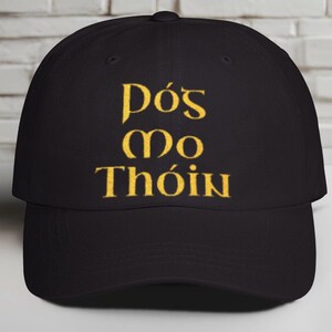 May include: A black baseball cap with a gold embroidered design that says "Dós mo Thóin".