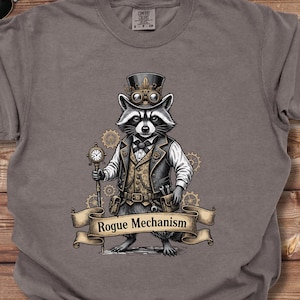 May include: A gray t-shirt featuring a raccoon dressed in steampunk attire, including a top hat and vest, holding a pocket watch. The text "Rogue Mechanism" is displayed on a banner below the raccoon.