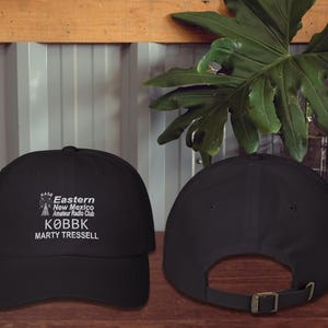 May include: Black baseball cap with white embroidered text that reads "Eastern New Mexico Amateur Radio Club KOBBK Marty Tressell". The cap is shown from the front and back.