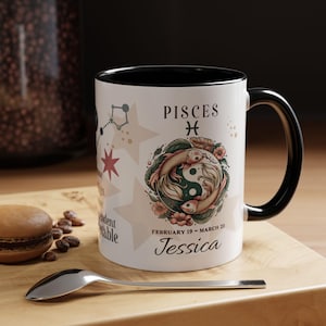 Puede incluir: Taza de cerámica blanca con borde y asa negros. La taza presenta un símbolo del zodíaco de Piscis con dos peces, estrellas y el texto "Piscis", "Febrero 19 - Marzo 20" y "Jessica".