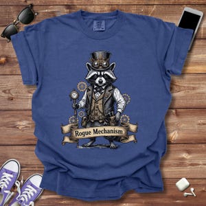 May include: Blue t-shirt featuring a raccoon in a steampunk outfit, complete with a top hat, goggles, and a pocket watch. The raccoon is standing in front of a banner that reads "Rogue Mechanism".