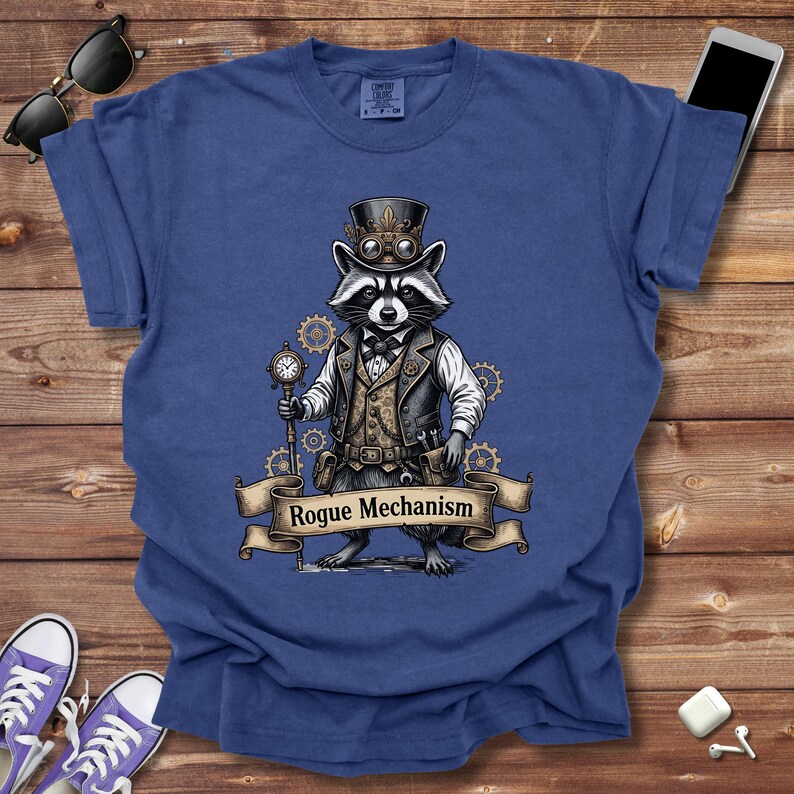 May include: Blue t-shirt featuring a raccoon in a steampunk outfit, complete with a top hat, goggles, and a pocket watch. The raccoon is standing in front of a banner that reads "Rogue Mechanism".