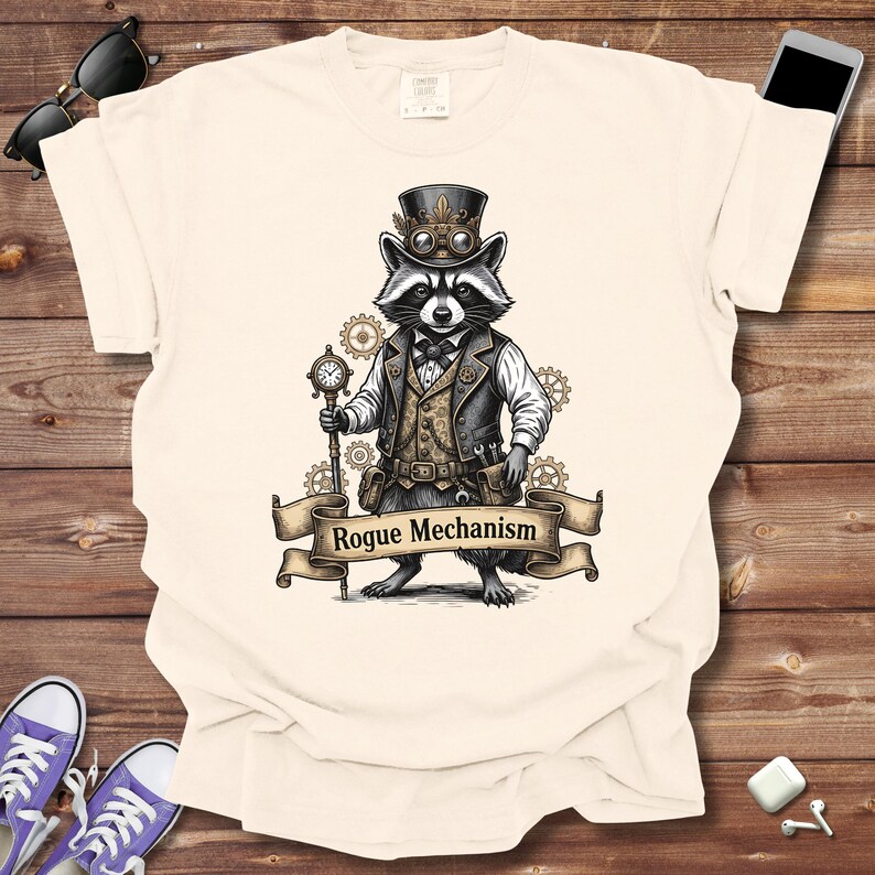 May include: Cream-colored t-shirt featuring a raccoon in steampunk attire, including a top hat, goggles, and vest. The raccoon holds a pocket watch and a banner that reads "Rogue Mechanism". Gears and cogs surround the raccoon, creating a unique design.