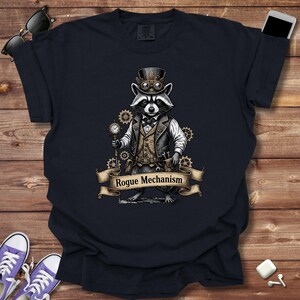 May include: Navy blue t-shirt featuring a raccoon in a steampunk outfit, complete with a top hat, goggles, and a pocket watch. The raccoon stands in front of gears with a banner that reads "Rogue Mechanism".