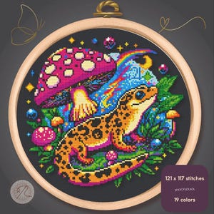 Può includere: Ricamo a punto croce in un telaio di legno. Il disegno presenta un geco colorato con macchie arancioni, un grande fungo rosa e un arcobaleno. Il testo sull'immagine dice "121 x 117 punti" e "19 colori".