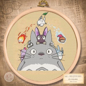 Peut inclure: Une broderie au point de croix représentant des personnages du film d'animation "Mon Voisin Totoro". Le motif comprend un grand Totoro gris, avec des personnages plus petits et des détails de différentes couleurs. La broderie est dans un cercle en bois.