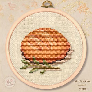May include: A cross-stitch pattern in a round wooden hoop featuring a round orange fruit with a textured surface and green leaves at the base. The design is stitched on light beige fabric with a grid pattern, measuring 42 by 36 stitches.