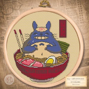 Puede incluir: Bordado de punto de cruz de un personaje de dibujos animados azul disfrutando de un cuenco de ramen. El personaje está en el centro, con un cuenco rojo de fideos, carne y un huevo cocido. El bordado está en un aro de madera.