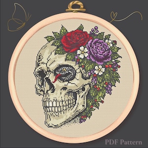 May include: Cross-stitch design featuring a skull adorned with red and purple roses, white flowers, and green foliage. The design is set within a wooden embroidery hoop. The words "PDF Pattern" are at the bottom.
