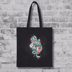 May include: Black tote bag with a teal and white dragon design, entwined with pink cherry blossoms. The dragon is highly detailed, set against a textured background. The bag has black handles.