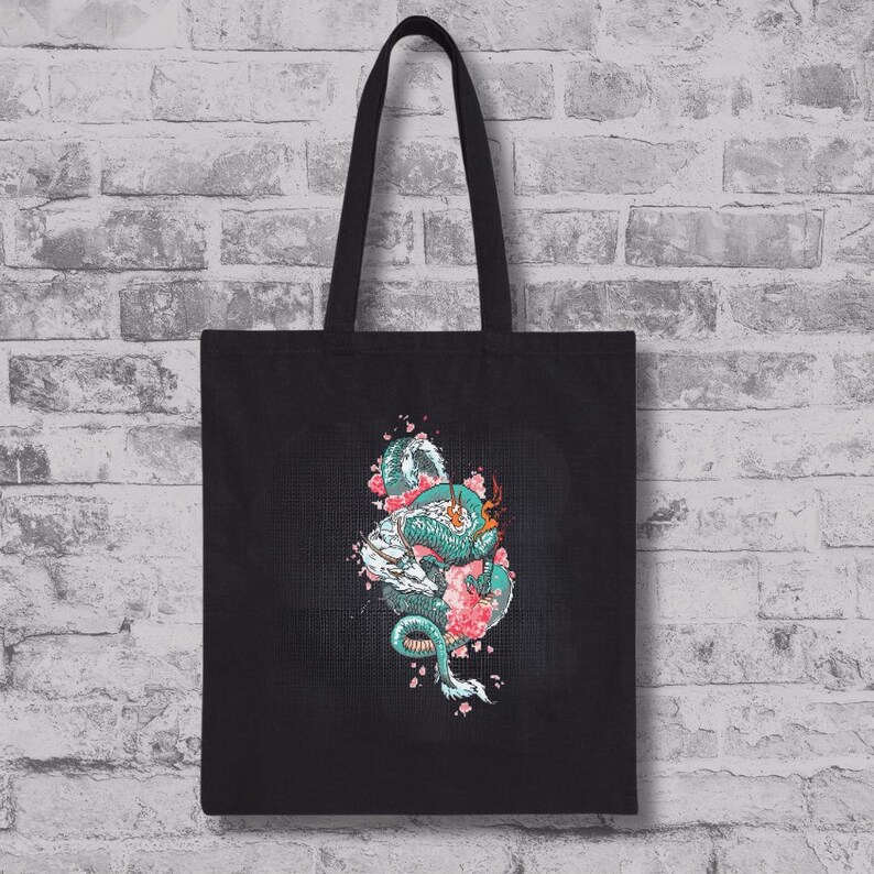 May include: Black tote bag with a teal and white dragon design, entwined with pink cherry blossoms. The dragon is highly detailed, set against a textured background. The bag has black handles.