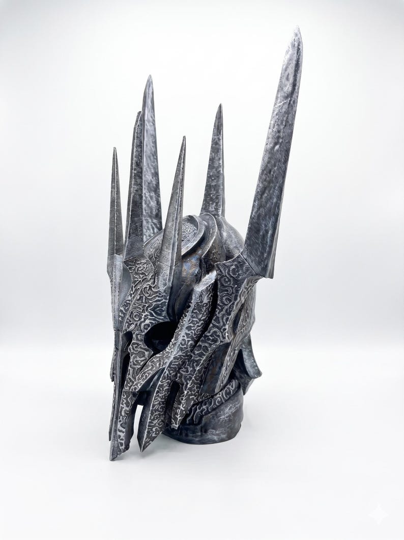 K&ouml;nnte beinhalten: Ein dunkler Metallhelm mit einer hohen, spitzen Krone und mehreren scharfen, vertikalen Dornen. Die Oberfl&auml;che ist mit komplizierten, ge&auml;tzten Rankenmustern verziert und weist ein verwittertes, abgenutztes Finish in Silber- und Anthrazitt&ouml;nen auf.