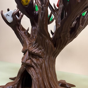 Pu&ograve; includere: Una torre per dadi a forma di albero, stampata in 3D, marrone, con un volto scolpito nel tronco. I rami dell'albero contengono vari dadi colorati, tra cui gialli, verdi, rossi e bianchi. La base dell'albero ha radici esposte.