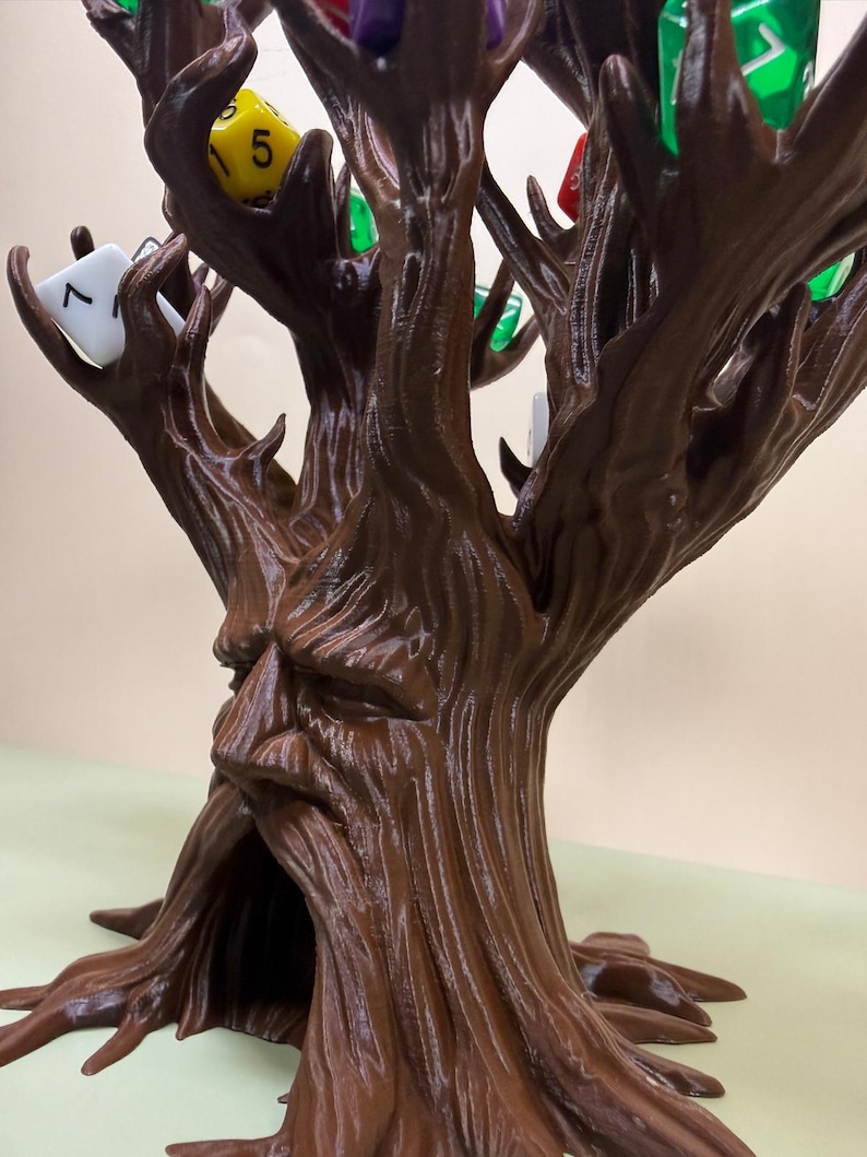 Pu&ograve; includere: Una torre per dadi a forma di albero, stampata in 3D, marrone, con un volto scolpito nel tronco. I rami dell'albero contengono vari dadi colorati, tra cui gialli, verdi, rossi e bianchi. La base dell'albero ha radici esposte.