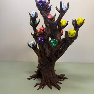 Pu&ograve; includere: Un porta dadi a forma di albero marrone con pi&ugrave; rami, ognuno dei quali tiene un dado colorato. I dadi sono di vari colori, tra cui viola, rosso, giallo, verde e bianco. L'albero ha un volto scolpito sul tronco.