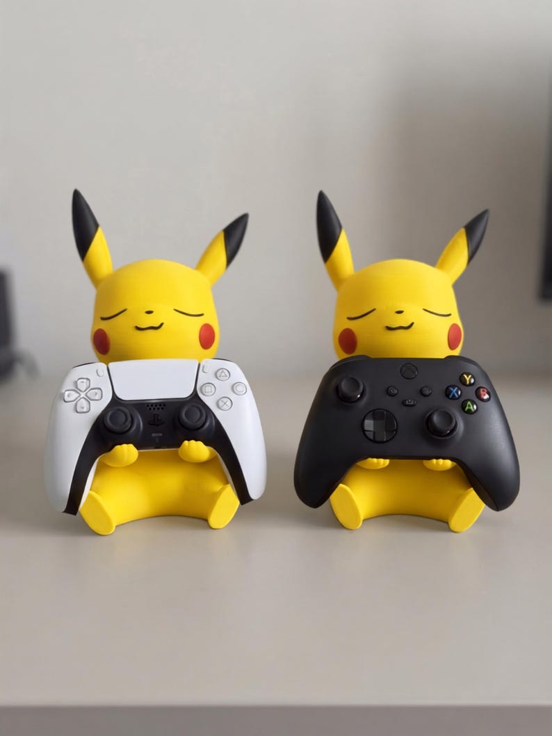 May include: Two yellow Pikachu figures with pointed ears and red cheeks, each sitting and holding a video game controller. One figure holds a white and black controller, while the other holds a solid black controller with colored buttons.