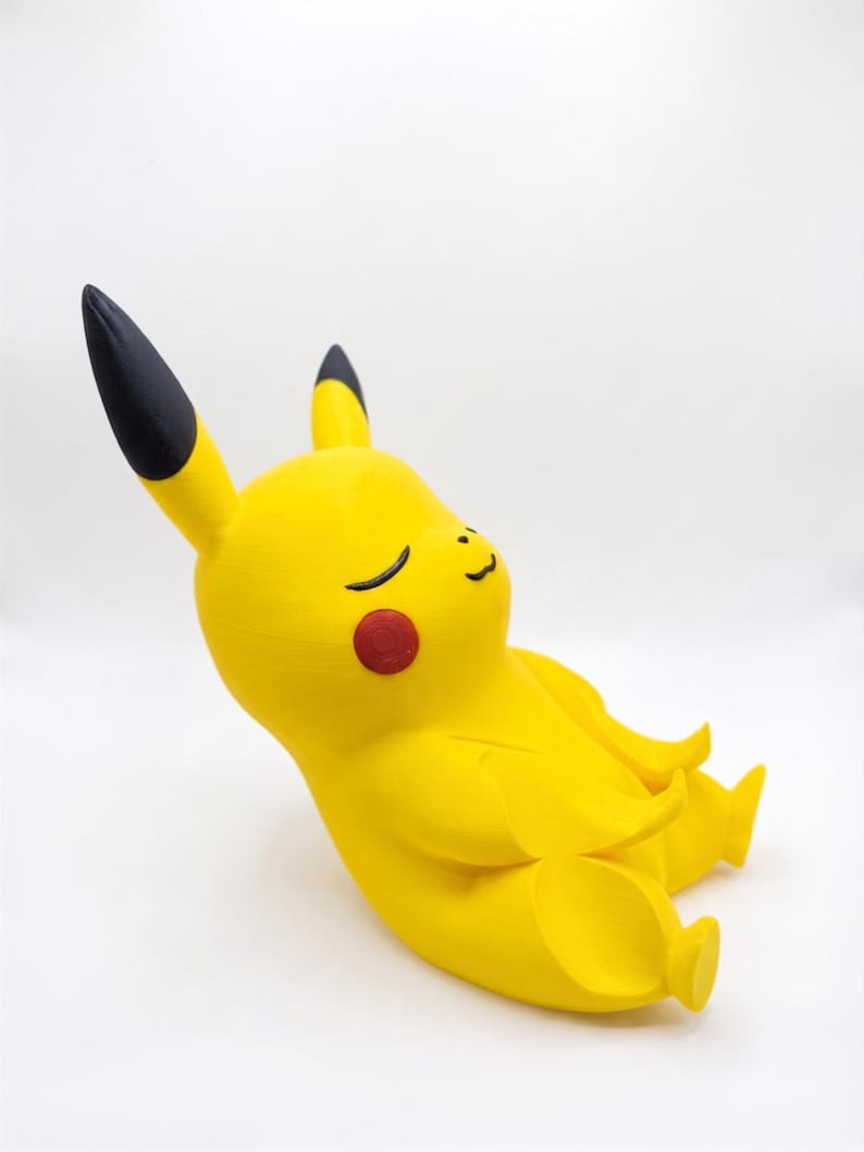 May include: A yellow Pikachu figurine in a seated, meditative pose with eyes closed and a small smile. The character features long ears with black tips, round red cheeks, and a smooth, matte finish, captured from a side-angle perspective.