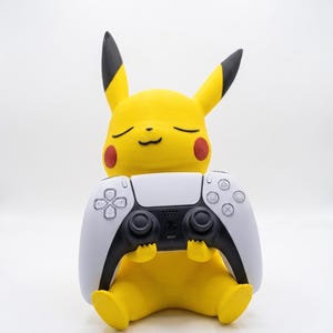 May include: A yellow Pikachu figure with black-tipped ears and red cheeks, sitting in a seated position while holding a white and black video game controller. The figure has a smooth, matte finish and a serene expression with closed eyes.