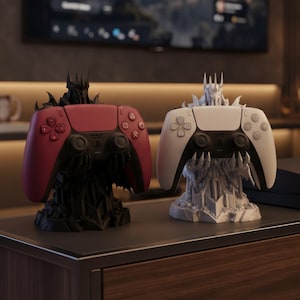 May include: Two gaming controller stands shaped like armored figures with spiked crowns. One stand is matte black holding a red controller, and the other is matte white holding a white controller. Both stands feature claw-like hands supporting the devices.