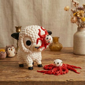 May include: A white sheep figurine with black ears and hooves, and a red octopus-like creature attached to its face. A smaller red octopus figurine is in front of the sheep. The figurines are on a wooden surface.