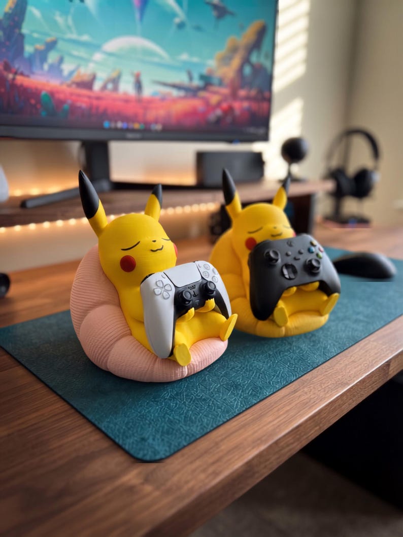 May include: Two yellow Pikachu figures with black-tipped ears and red cheeks, each sitting in a textured pink beanbag chair. One figure holds a white and black game controller, while the other holds a solid black game controller.