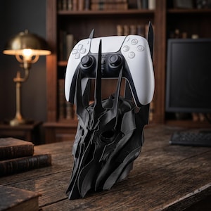 Könnte beinhalten: Ein schwarzer, stacheliger Controller-Ständer in Helmform, der einen weißen und schwarzen kabellosen Game-Controller hält. Der Ständer verfügt über scharfe, längliche vertikale Vorsprünge und eine dunkle, texturierte Oberfläche.