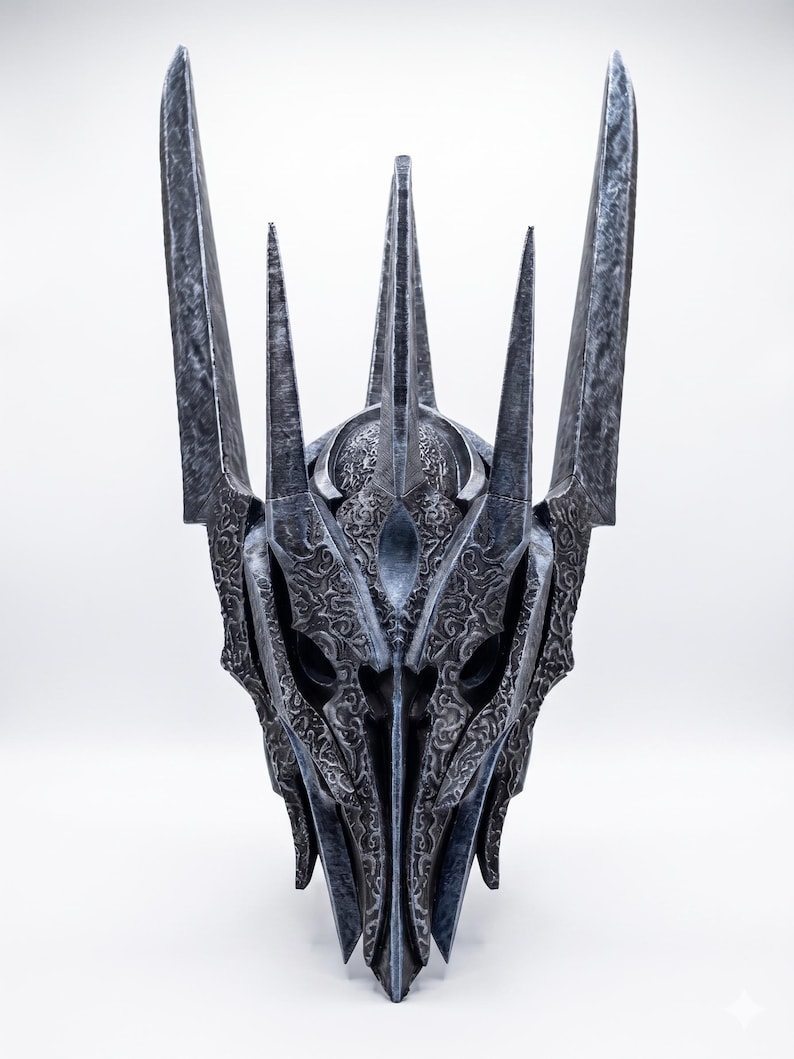 K&ouml;nnte beinhalten: Ein dunkelgrauer, metallisch wirkender Helm mit einer hohen, spitzen Krone und mehreren vertikalen Zacken. Die Oberfl&auml;che ist mit komplexen, erhabenen Wirbelmustern und Texturen bedeckt, die ihm ein gealtertes, verwittertes Aussehen mit scharfen Kanten verleihen.
