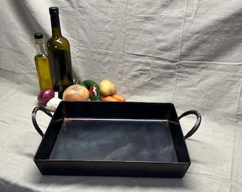 May include: A black metal rectangular baking pan with two handles. The pan is empty and sitting on a white fabric surface.