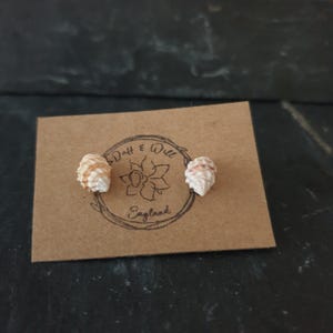 以下が含まれることがあります： 茶色のカードに「Drift & Will England」という文字が書かれた、小さな白い貝殻のイヤリングのペアです。