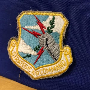 May include: A white ceramic mug with a black handle and the text "But First, Coffee" in a bold, black font. The mug is set against a blurred background, suggesting a cozy setting.