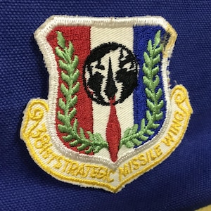 May include: Embroidered patch featuring a shield design with red, white, and blue vertical stripes. The patch includes a black and white graphic, green laurel branches, and the text "301st STRATEGIC MISSILE WING" in yellow.