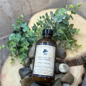 Puede incluir: Una botella de vidrio marr&oacute;n con una etiqueta negra y una tapa negra. La etiqueta dice "The Velvet Men's Edition" y "Vetiver and Teakwood Body Wash". Tambi&eacute;n dice "Shake Before Use", "100% Natural Ingredients", y "8 fl oz".