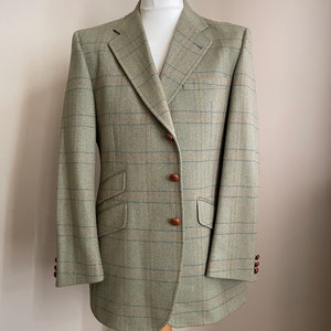 May include: A green tweed blazer with a brown button closure and a subtle plaid pattern.