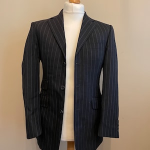 Könnte beinhalten: Ein schwarzer Nadelstreifenblazer mit einem Knopfverschluss und zwei Pattentaschen.