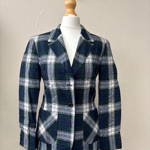 Può includere: Blazer a quadri verdi, blu navy e bianchi, esposto su un manichino. La giacca presenta un colletto a revers, una chiusura con un bottone e due tasche anteriori. Le maniche hanno polsini con bottoni.