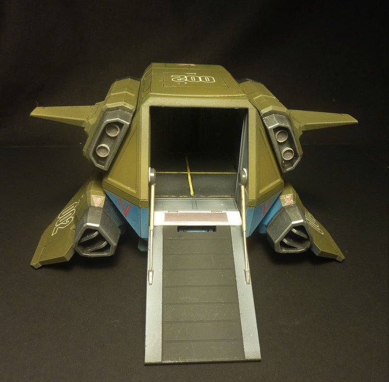 Puede incluir: Un veh&iacute;culo de transporte de juguete de estilo militar en verde oliva, azul y gris. El veh&iacute;culo tiene una bah&iacute;a de carga abierta con una rampa extendida. La parte superior del veh&iacute;culo tiene el n&uacute;mero "200" impreso. Tiene puertos de escape dobles.