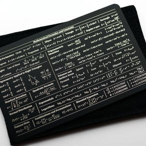 May include: A black card with gold lettering containing mathematical formulas and constants. The card includes formulas for areas and perimeters, triangles, trigonometry, standard deviation, quadratic formula, exponentials, logarithms, combinations and permutations, and binomial expansion.