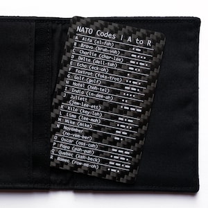 May include: A rectangular card with a black carbon fiber pattern featuring the text NATO Codes A to R, listing letters A through R with their corresponding phonetic words, pronunciations, and Morse code symbols, tucked into a black fabric sleeve.