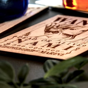 Puede incluir: Posavasos de madera con un dise&ntilde;o grabado con l&aacute;ser de un personaje de la serie de anime One Piece. El posavasos muestra la palabra &laquo;WANTED&raquo; y &laquo;NAMI&raquo; con una cantidad de recompensa. La madera es de color marr&oacute;n claro.